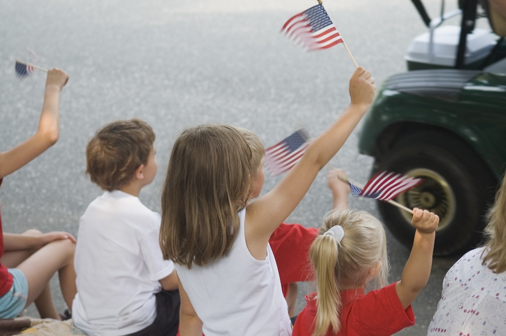 Family holding flags watching golf cart parade